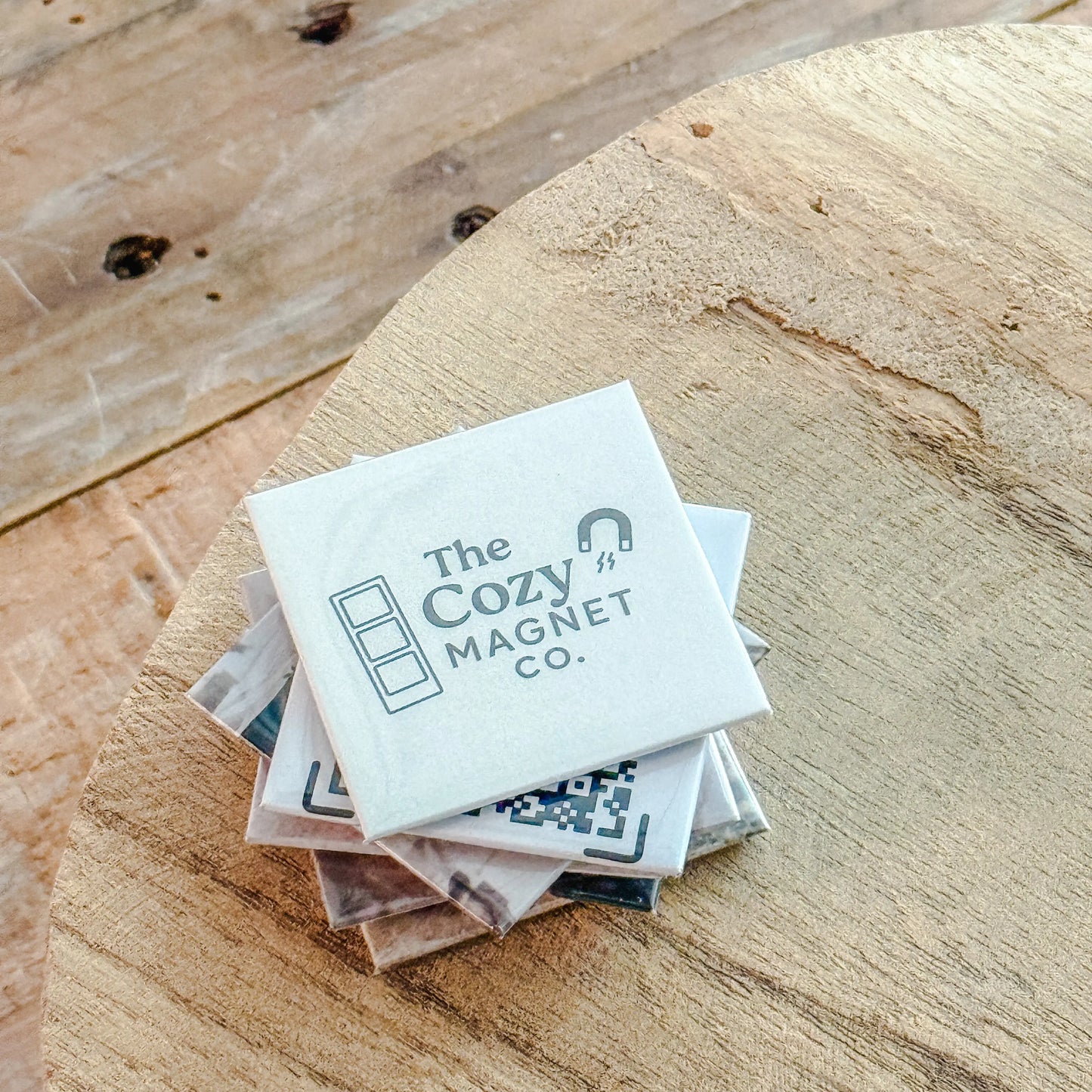 Stack of 'The Cozy Magnet Co.' products on a wooden surface