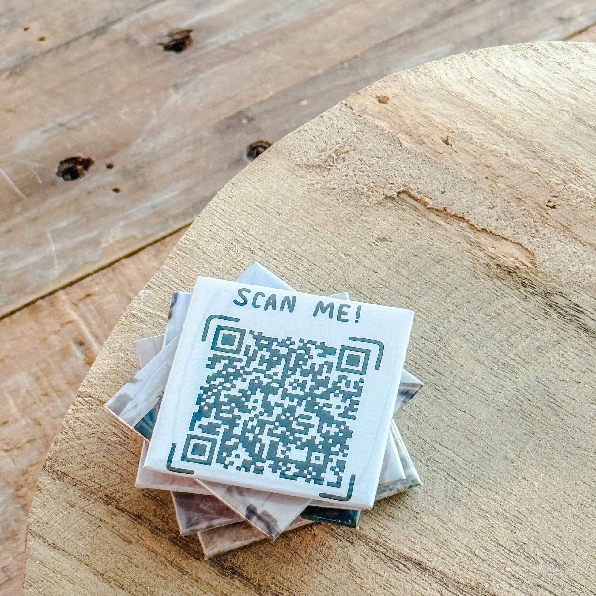 Stack of custom square magnets with QR code and 'Scan Me!' text on a wooden surface
